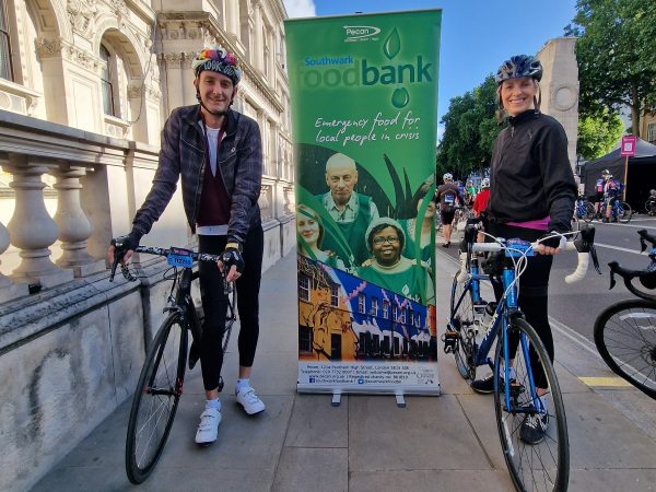 A woman and a man ready to cycle long distant infront of a banner that reads Southwark Foodbank