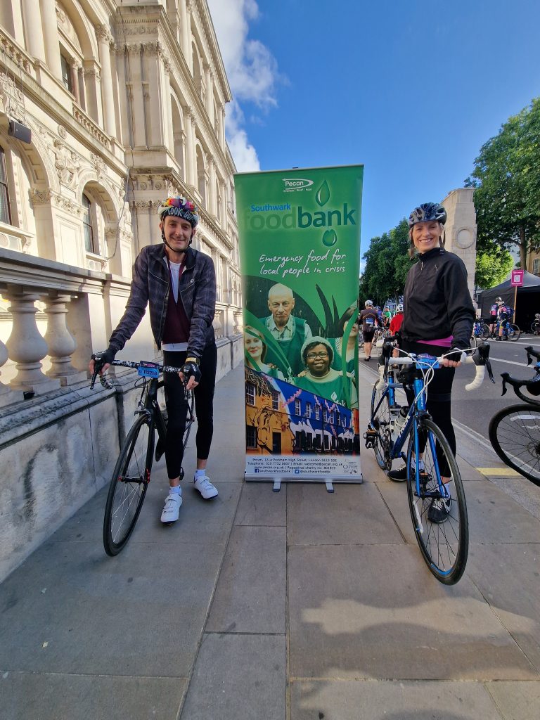 A woman and a man ready to cycle long distant infront of a banner that reads Southwark Foodbank