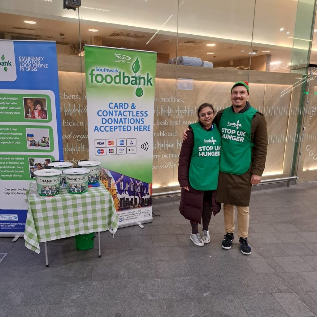 Two people standing with bibs next to foodbank banners and buckets