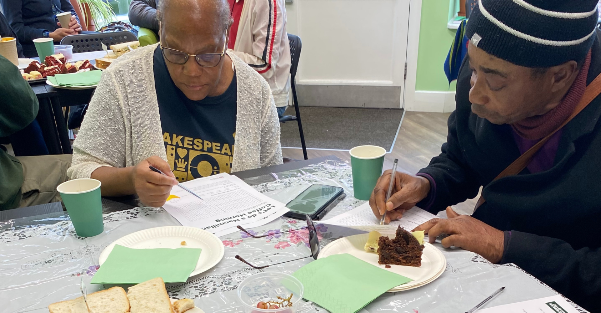 Two black people at a table writing with food around them
